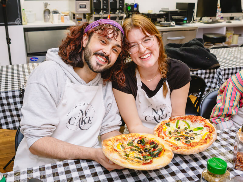 Smiling couple holding pizzas in a pizza class 